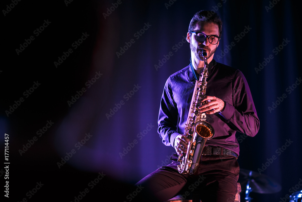 Obraz premium Saxophonist playing on a stage. Pink and blue lighning. Black background