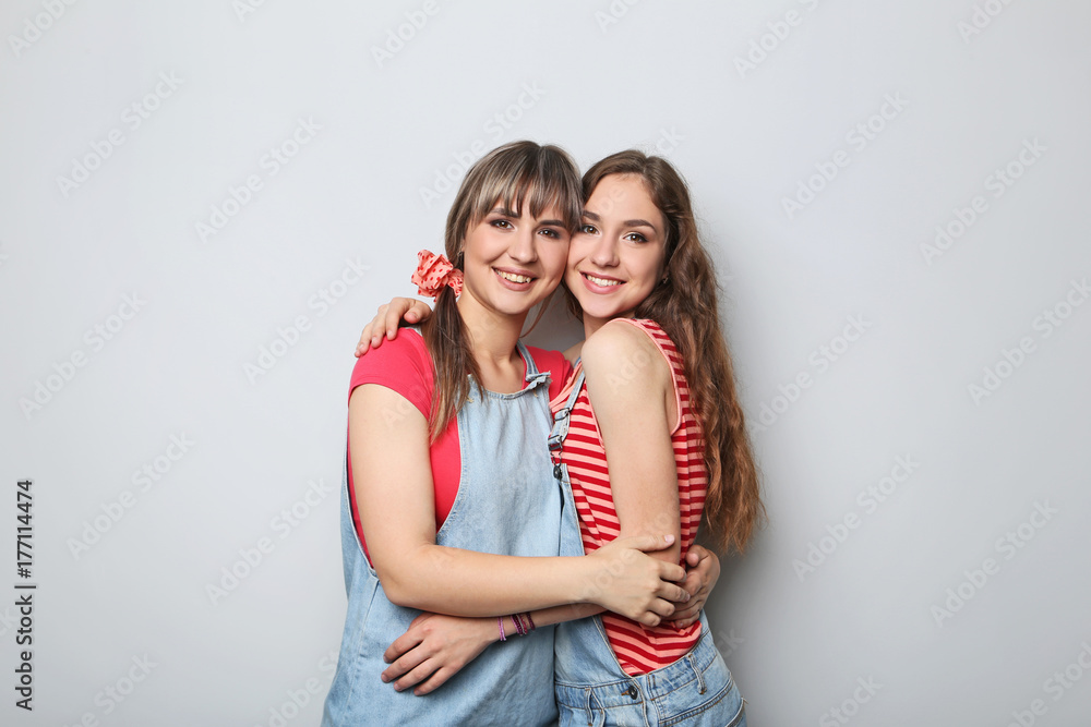 Two young woman hugging each other on grey background Two young woman hugging each other on grey background