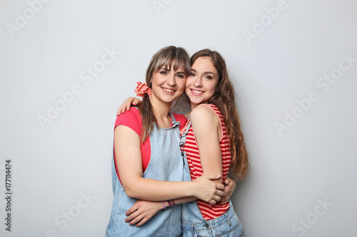 Two young woman hugging each other on grey background
