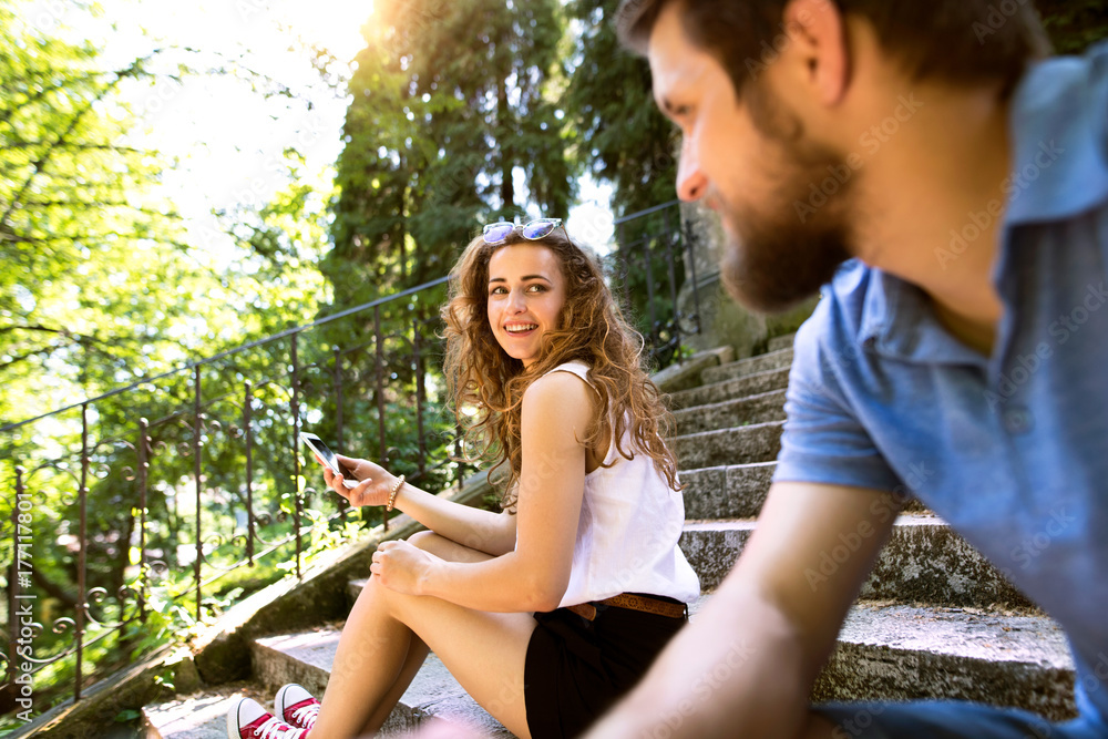 Young couple with smartphone sitting on stairs in town.