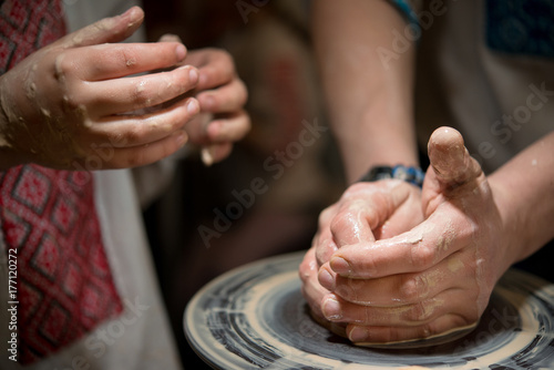 Teacher man teaches a child how to make a ceramic plate on the potter's pile. Close-up of child's hands and masters.