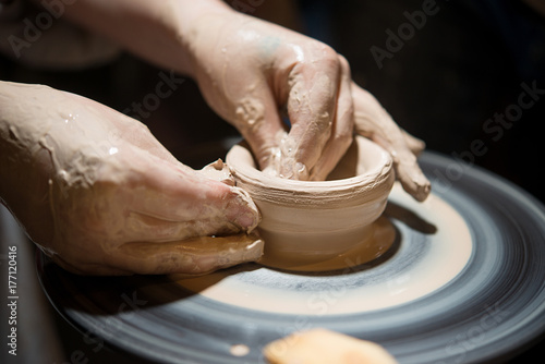 Teacher man teaches a child how to make a ceramic plate on the potter's pile. Close-up of child's hands and masters.