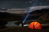 Man tourist with flashlight near his camp tent at night.
