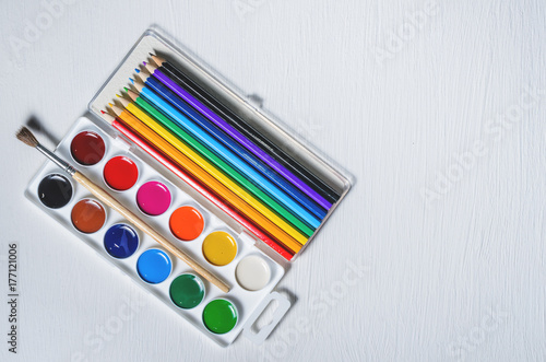 Bright colored watercolor paints and pencils, top view, white background.