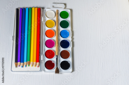 Bright colored watercolor paints and pencils, top view, white background.