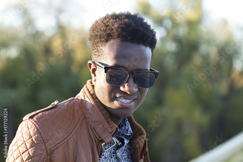 Handsome young black man in sunglasses and a leather jacket on a fall day