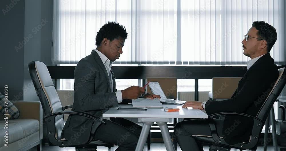 two young businessman talking at desk in office. European and African businessmen two young businessman talking at desk in office. European and African businessmen