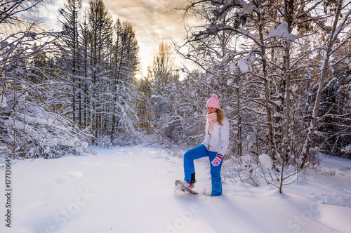 Winter sport activity. Woman with snowshoes on fluffy snow in forest. Beautiful landscape with coniferous trees and white snow. photo