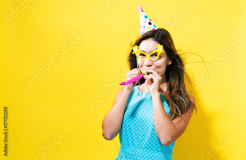 Fotografi Young woman with party hat with noisemaker on a yellow background