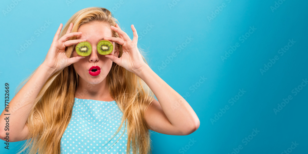 Happy young woman holding kiwis on a solid background