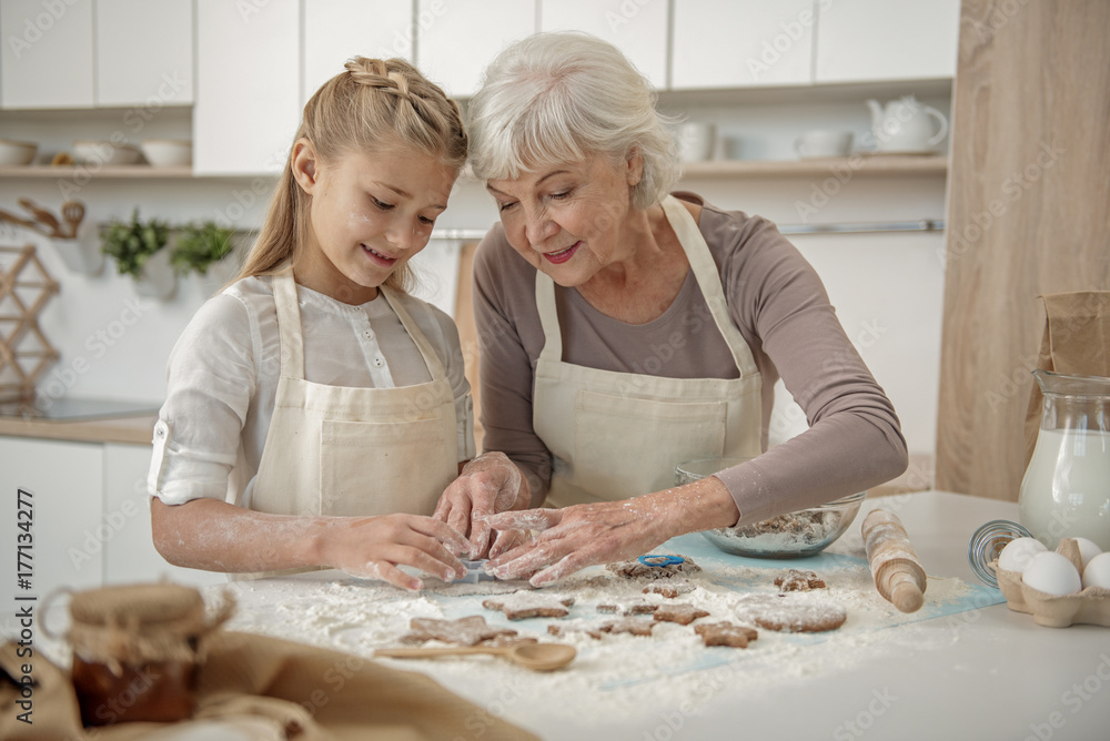 Cheerful grandchild learning to make pastry in kitchen - obrazy, fototapety, plakaty 