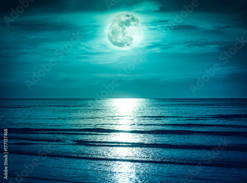 Colorful sky with dark cloud and bright full moon over seascape.