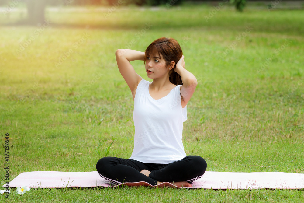 A pretty thai woman sitting on a mat and gathering her hair to practice yoga in park.