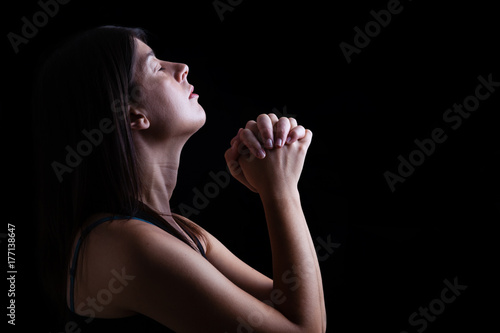Close up of a faithful woman praying under a divine or celestial light, hands folded in worship, head up and closed eyes in religious fervor. Concept for religion, faith, prayer and spirituality.
