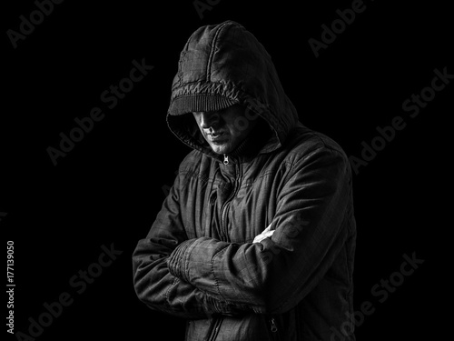 Lonely, depressed and fragile man hiding face, arms crossed and standing in the darkness. Low key, black background. Concept for loneliness, depression, sadness and mental health issues
