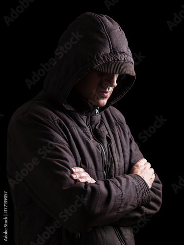 Lonely, depressed and fragile man hiding face, arms crossed and standing in the darkness. Low key, black background. Concept for loneliness, depression, sadness and mental health issues