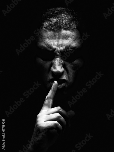 Fotografie Furious mature man with an aggressive look making the silence sign in a violent and threatening way