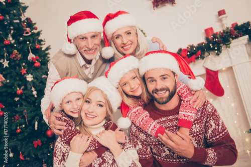 Six beautiful caucasian relatives embrace, married couples, excited siblings, grandad, granny, in knitted cute traditional x mas costumes, .pine firtree, home interior, stockings