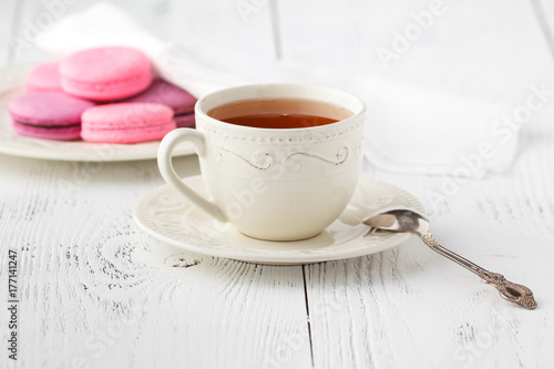 Colorful French macaroons and cup of tea on a rustic wooden background, selective focus