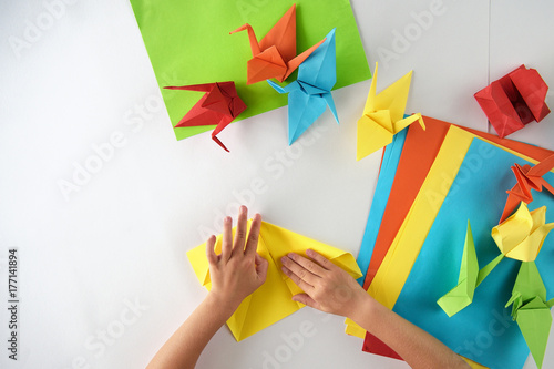 Children's hands do origami from colored paper on white background. lesson of origami