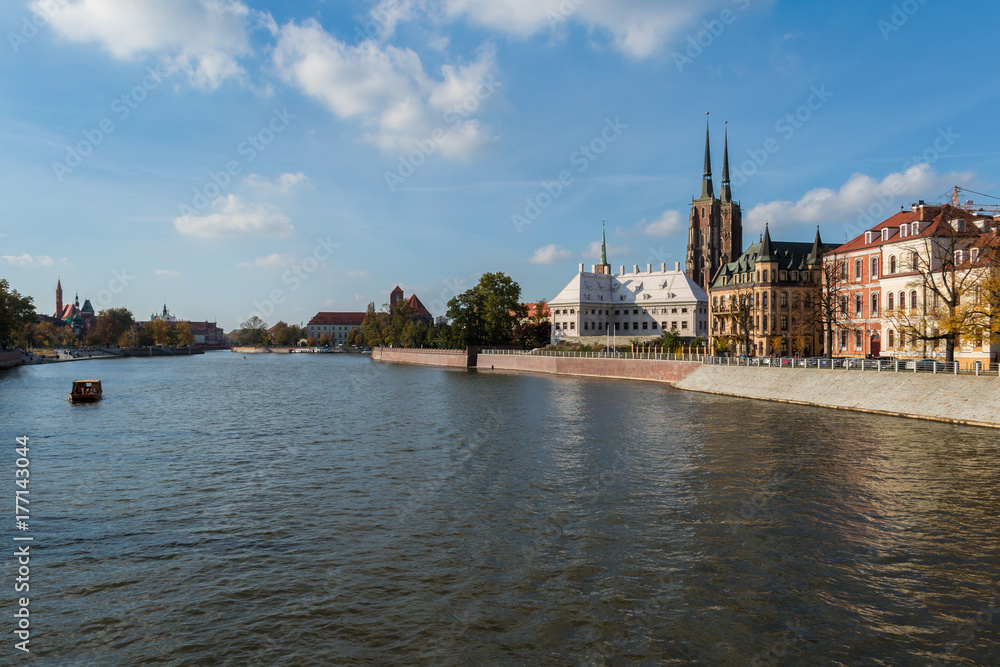 Boat sailing on the Oder river alongside the Cathedral Island in Wroclaw on a sunny day under the blue sky with white clouds