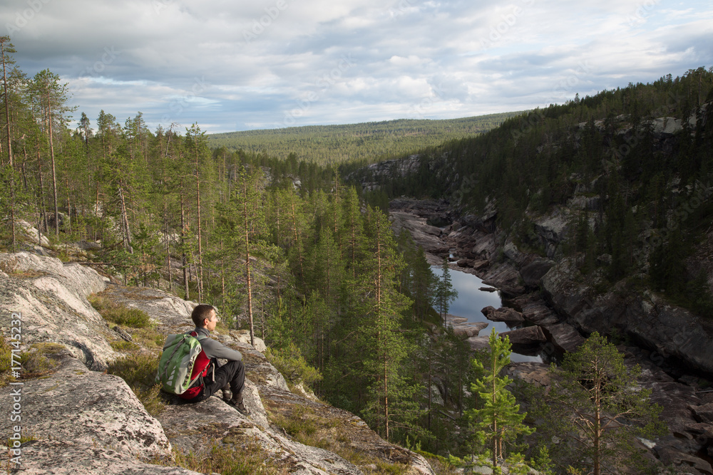 Young hiker sitting at a rocky canyon near by Porjus, Sweden, summer 