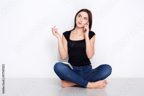 Woman talks on phone, sitting on home floor