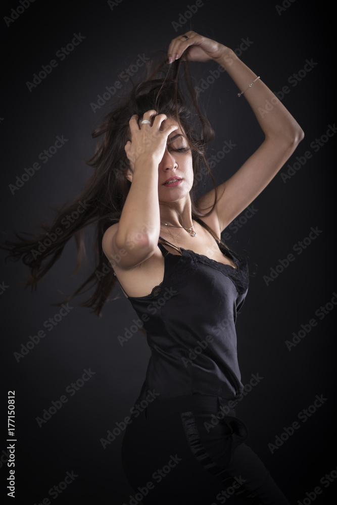 Portrait of the beautiful young brunette woman with long black hair posing standing over dark background