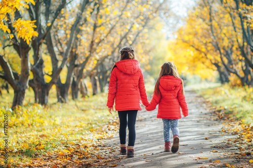 two sisters are walking together in an autumn park. Two girls holding hands walking outdoors in autumn