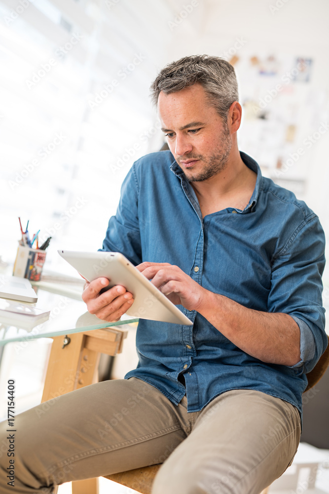 Sitting at his desk a handsome man using a digital tablet Sitting at his desk a handsome man using a digital tablet