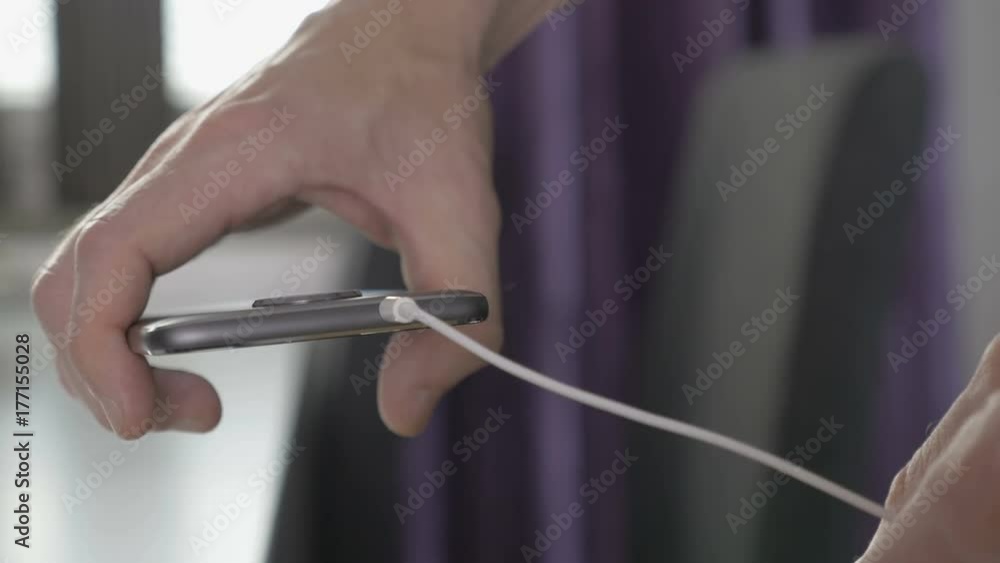 Man plugging in wire to headphone jack on a smartphone Man plugging in wire to headphone jack on a smartphone
