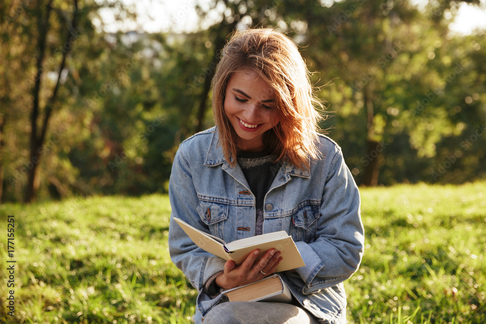 Cheerful young woman in jeans jacket reading a book in sunny park Cheerful young woman in jeans jacket reading a book in sunny park