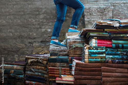 Education, concept. A young woman climbs up the stairs of books