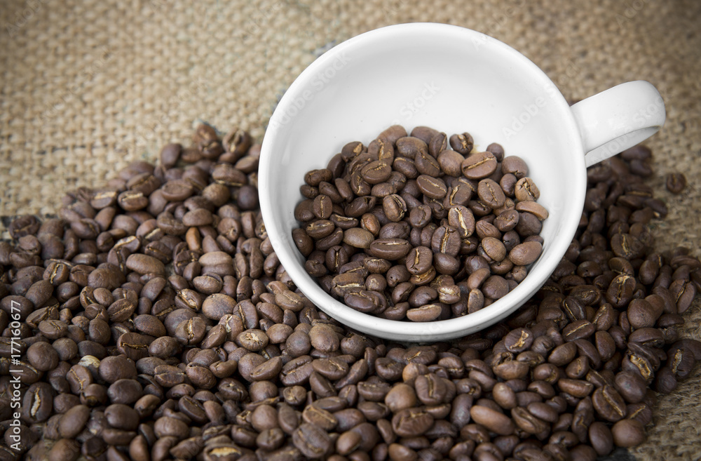 Fototapeta premium arabica coffee beans in coffee cup with sack cloth background.roasted coffee beans pattern