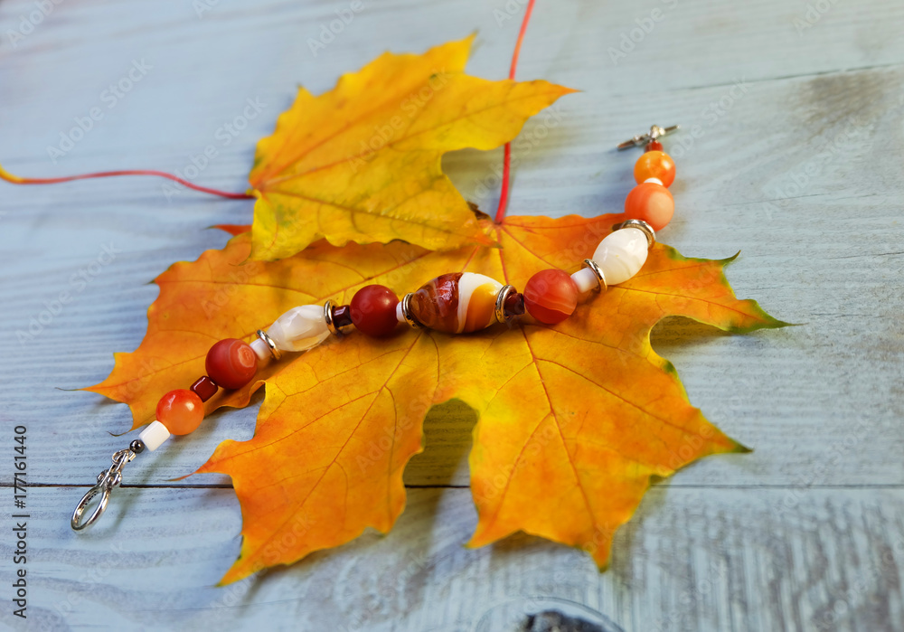 Bracelet made of Murano glass and carnelian on a background of autumn leaves  on a blue wooden table. Stock Photo | Adobe Stock
