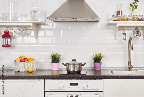 Interior of a light kitchen in the apartment. Bright home interior decoration items, fruit, flowers in a pot, steel hood. Bright ready-made picture for your individual design 