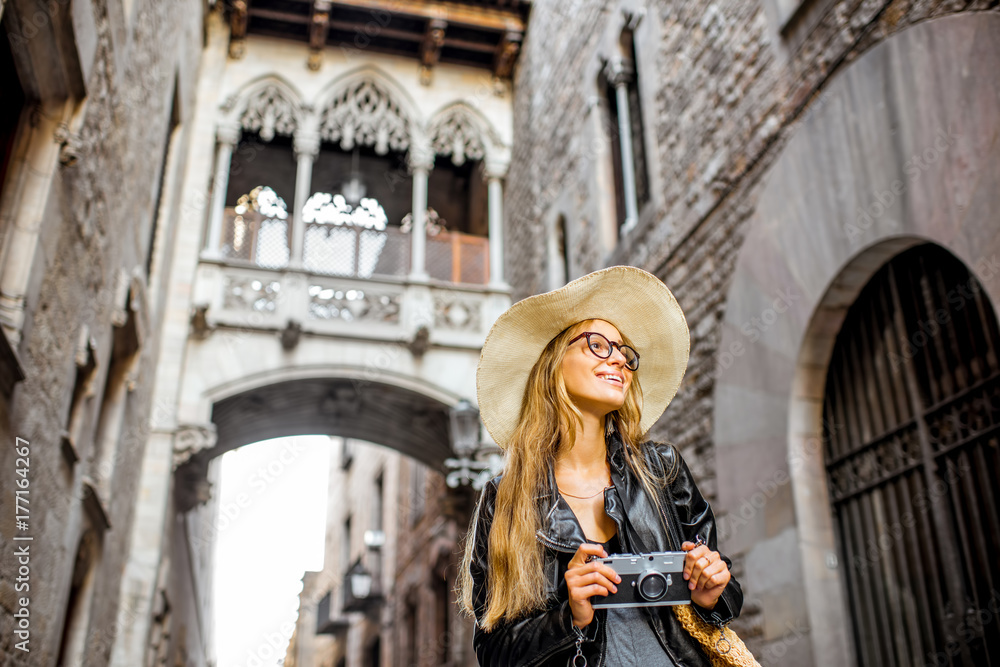 Fototapeta premium Young woman tourist in hat standing with photo camera in front of the famous bridge of sighs in Barcelona old town