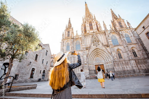 Young woman tourist photographing with phone famous saint Eulalia church during the morning light in Barcelona city