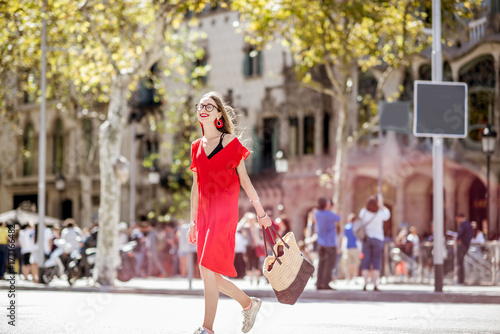 Lifestyle portrait of a beautiful woman in red dress crossing the central city avenue in Barcelona