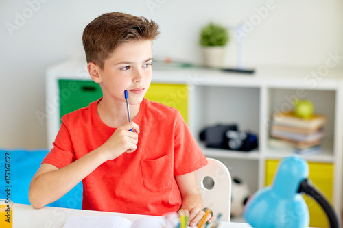 student boy with pen and notebook thinking at home