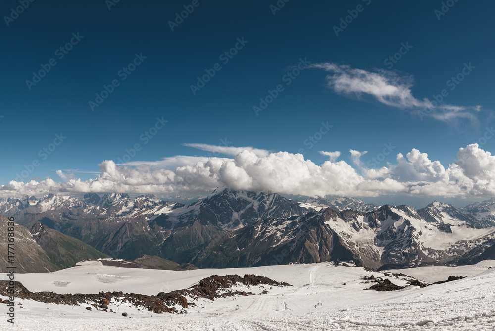 Dark blue sky with clouds on the rocky peaks of the mountains covered with glaciers and snow