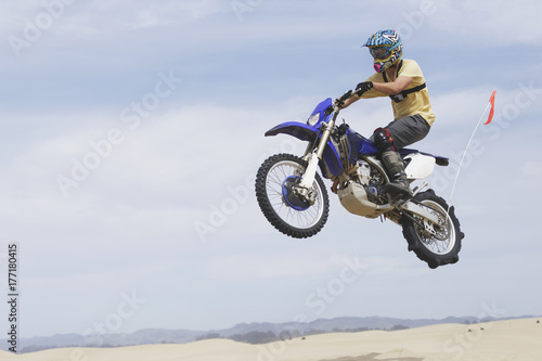 Young man jumping a dirt bike on the sand dunes photo