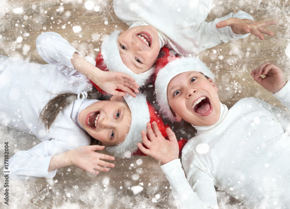 happy child lying together on wooden background, dressed in christmas Santa hat and having fun, winter holiday concept, snow decoration happy child lying together on wooden background, dressed in christmas Santa hat and having fun, winter holiday concept, snow decoration