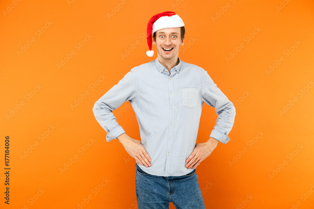 Emotional man in red christmas cap, hands on belt, toothy smile and looking at camera. Emotional man in red christmas cap, hands on belt, toothy smile and looking at camera.
