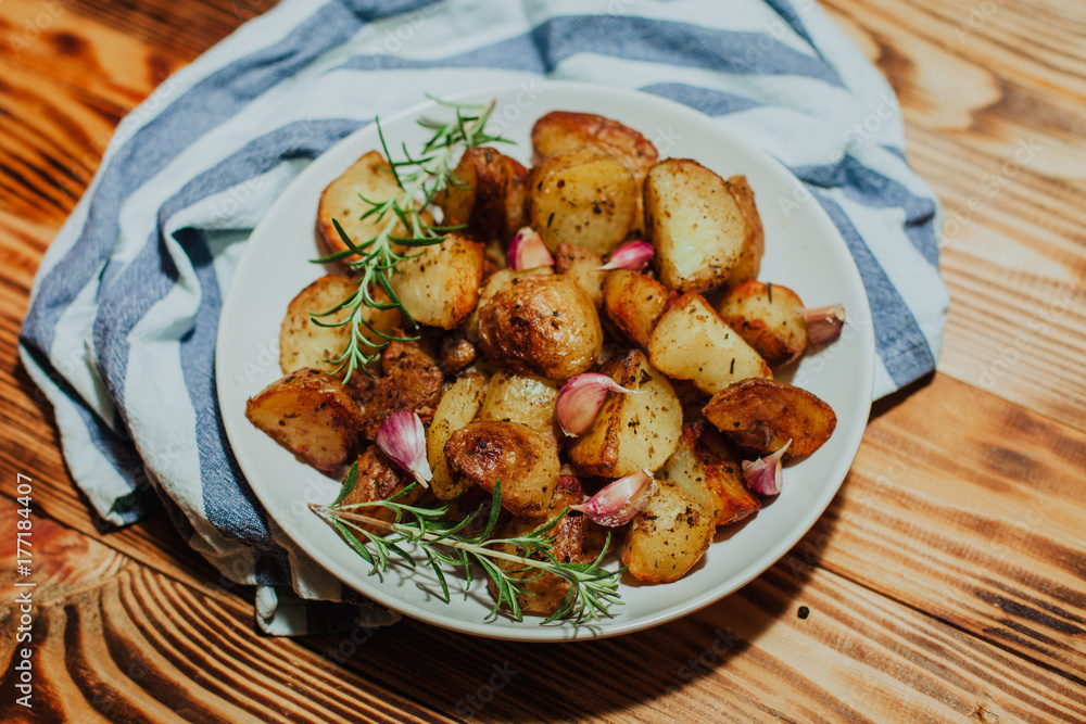 Roasted potato in white plate on wooden background with rosemary and garlic