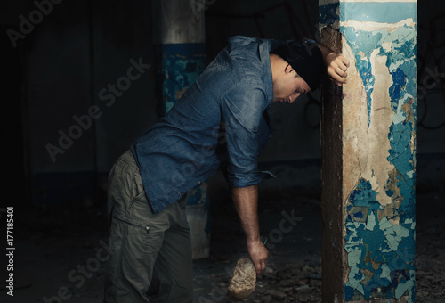 Hopeless man with bottle of alcohol in abandoned building