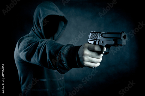 Hooded man with a gun in the dark 