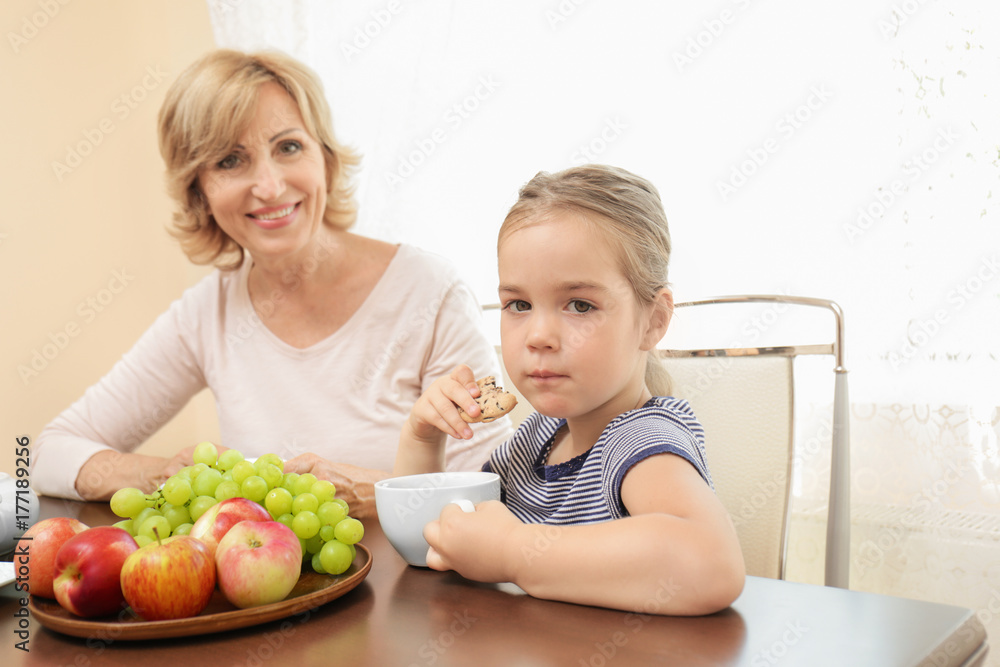 Cute little girl and her grandmother sitting at table Cute little girl and her grandmother sitting at table