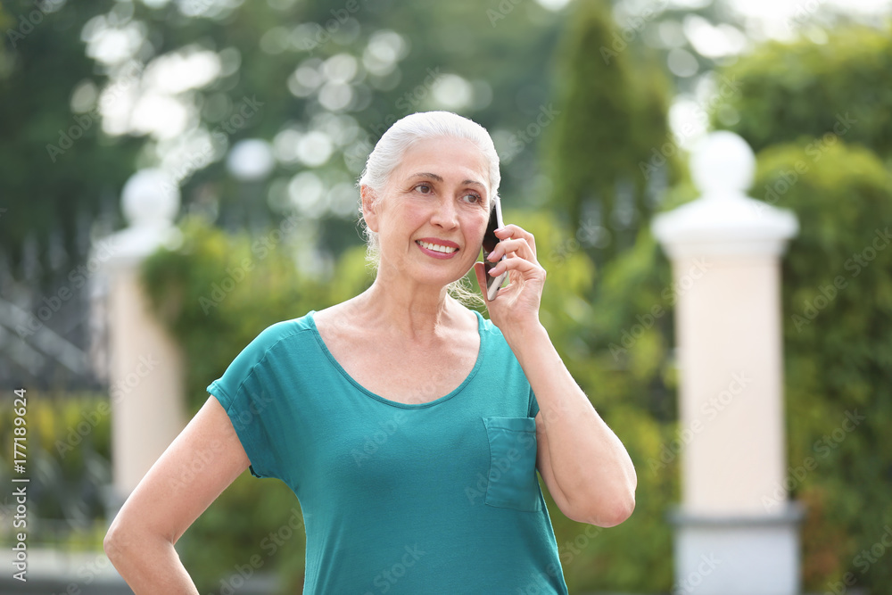 Fototapeta premium Beautiful senior woman talking on mobile phone outdoors
