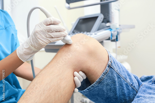 Doctor conducting ultrasound examination of patient's knee in clinic